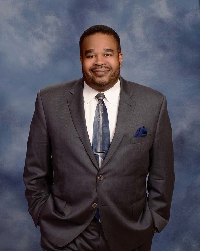 A man in a suit and tie standing with his hands in his pockets.